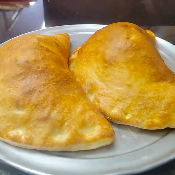 Two golden-brown calzones, fresh from the oven, rest on a silver plate.