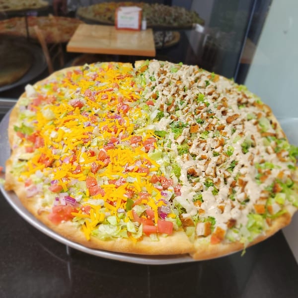A large pizza split with taco toppings on one half and chicken Caesar salad on the other.