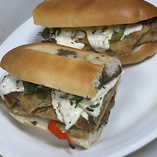 Two Italian sandwiches on a white plate, filled with meat, white sauce, and green herbs.