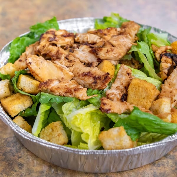 Midways De La Roma's Italian chicken Caesar salad with croutons in a foil takeout container.