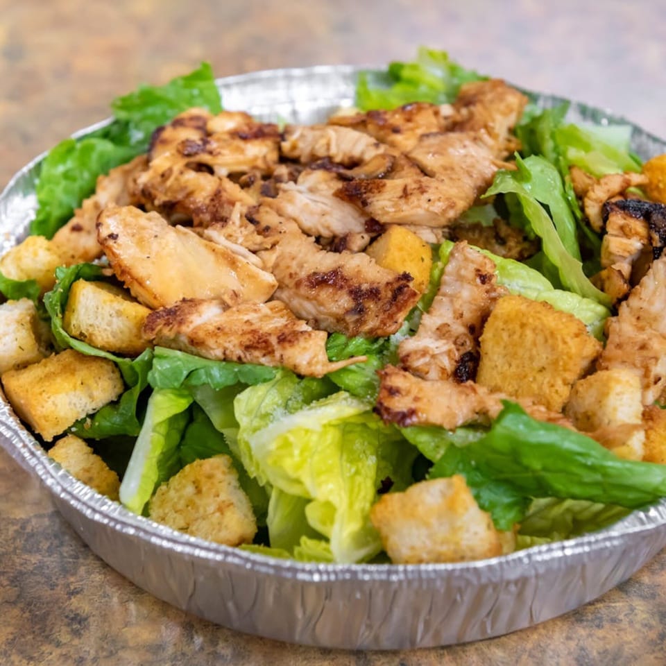 Midways De La Roma's Italian chicken Caesar salad with croutons in a foil takeout container.